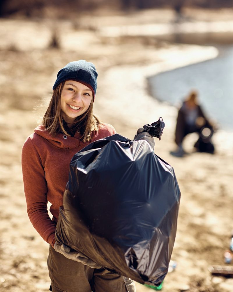 Happy teenage volunteer with garbage bag full of trash she picked up on the beach.